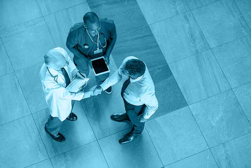 High angle view of senior doctor shaking hands to representative of pharmaceutical companies. Top view of businessman shaking hands with physician in a hospital. Businessman conclude an agreement with doctor.